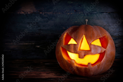 Orange pumpkin carved into creepy and funny Jack o Lantern w/ glowing eyes on dark background. All hallows night. Copy space, close up, top view. Halloween party decoration. Trick or treat concept.