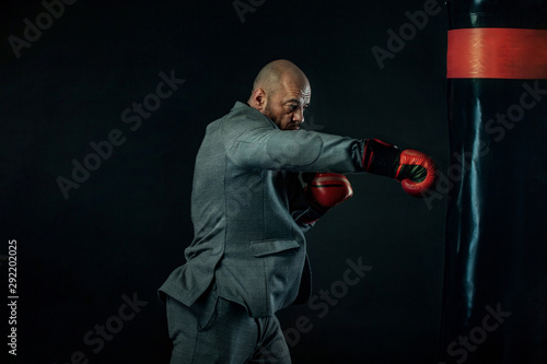 Businessman and sportsman in suit, man boxer in gloves with boxing punching bag. Trainings and motivation with fitness coach. © Mike Orlov