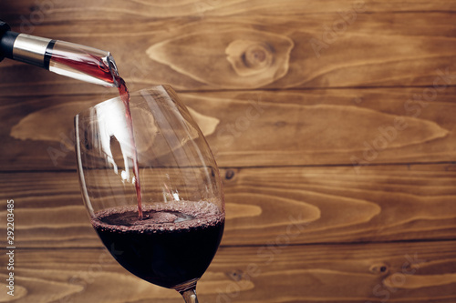 Pouring red wine into a vine glass with decanter or aerator attached to bottle neck. Rustic wooden background. Place for text. Copy-space. photo