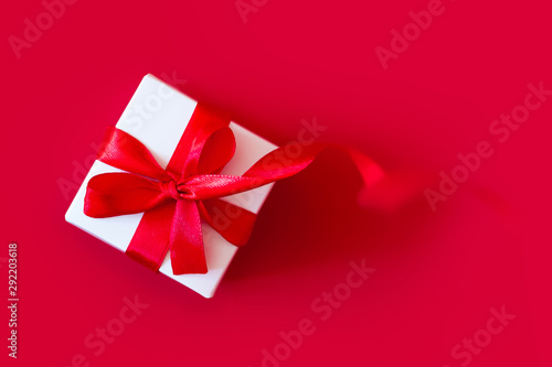 White box with a red ribbon on a red background, top view, copy space. Greeting card concept