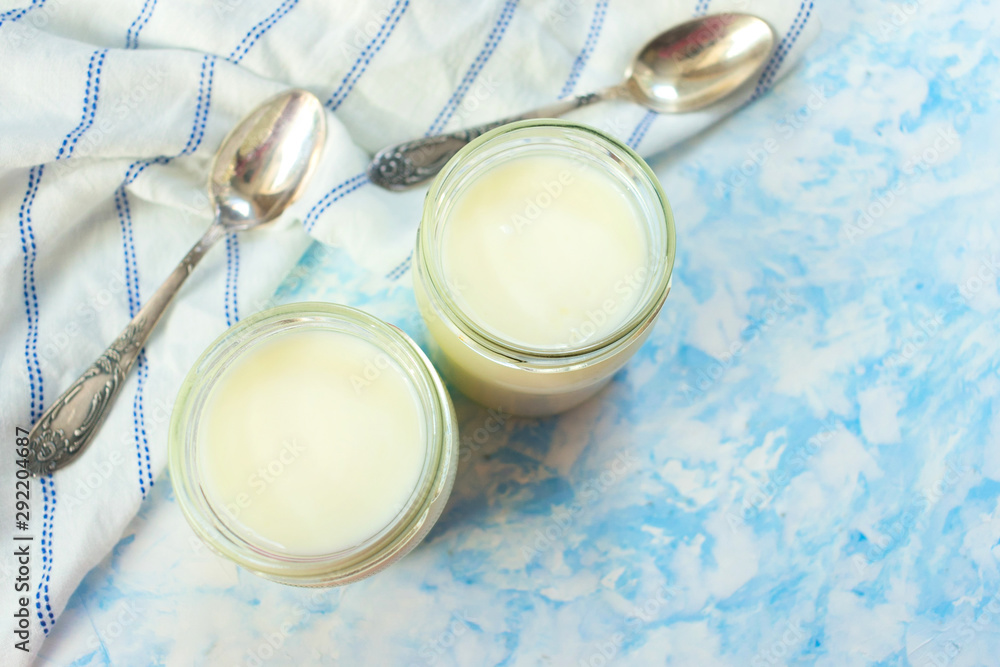 Greek yogurt in glass jars with spoons on a blue background. Top view. Copy space. Greek yogurt in glass jars with spoons on a blue background. Top view. Copy space.