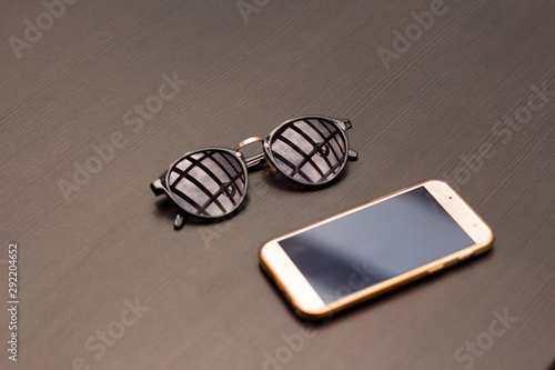 A gold cell phone and sunglasses lie on a wooden table.
