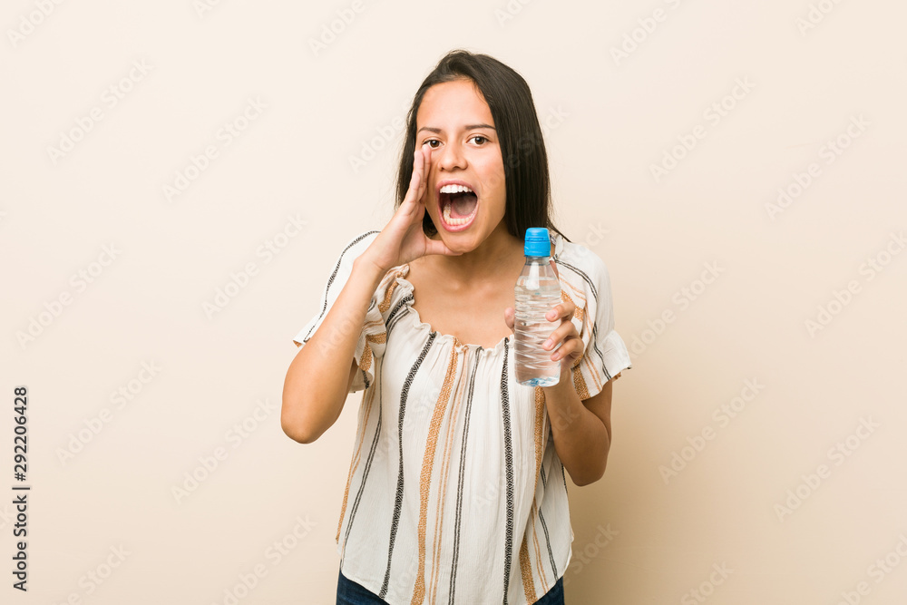 Young hispanic woman holding a bottle of water shouting excited to front. Young hispanic woman holding a bottle of water shouting excited to front.