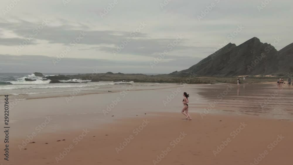 Aerial drone view young woman running on a beach on Praia de Amoreira, Portugal Aerial drone view young woman running on a beach on Praia de Amoreira, Portugal