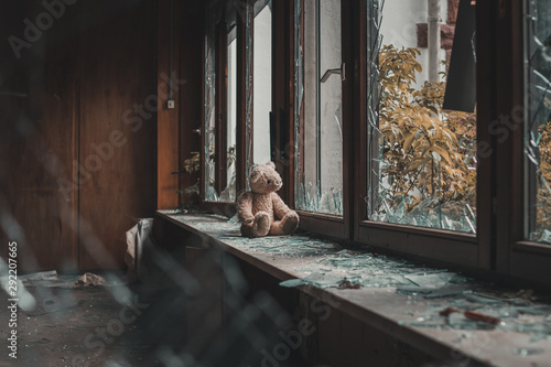 teddy bear sitting on windowsill. Looking through broken window glass