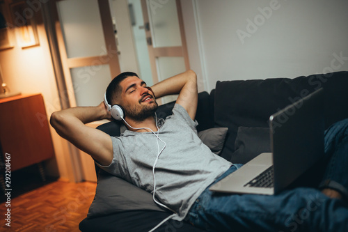 man relaxing at his home listening music and using laptop computer