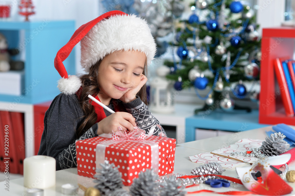 Happy girl in Santa hat sitting with Christmas present Happy girl in Santa hat sitting with Christmas present