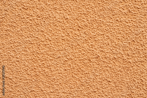 A fragment of the wall of the house. Plaster of beige sand color. Granulated surface