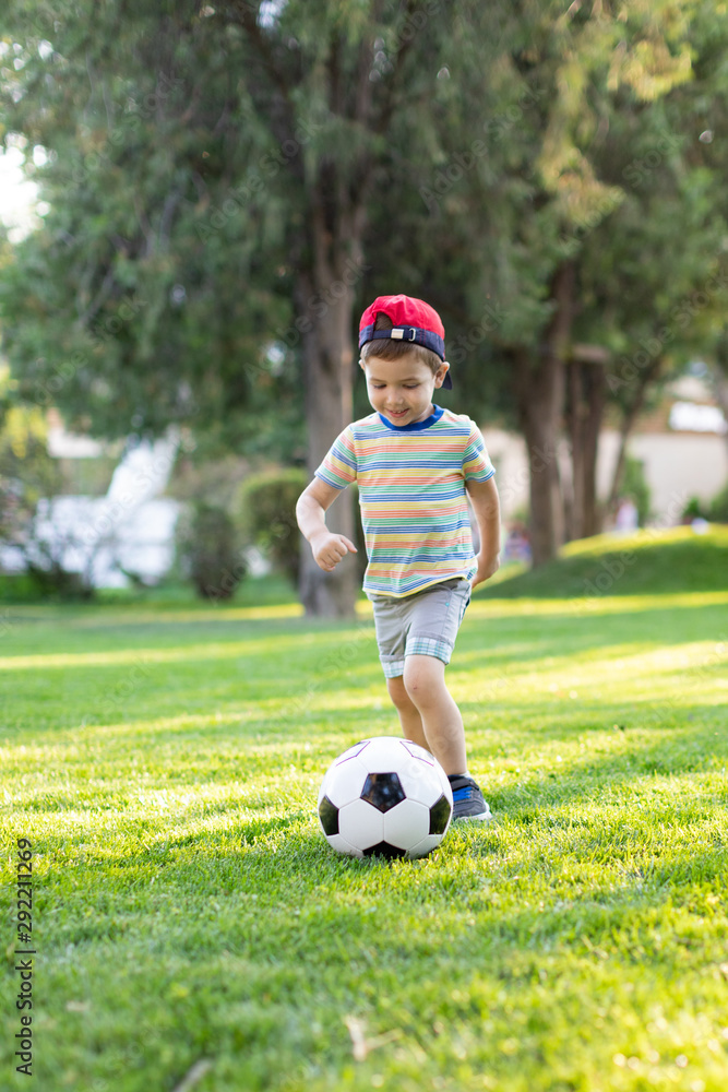 Little boy happy kid playing football and ready to kick the ball on green grass with copyspace Little boy happy kid playing football and ready to kick the ball on green grass with copyspace