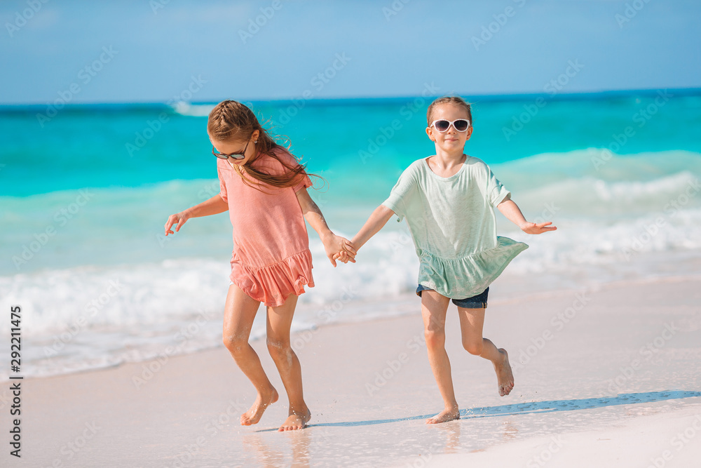 Adorable little girls have fun together on white tropical beach