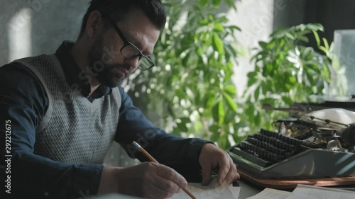 Wallpaper Mural Old fashion: a man in glasses with a beard works sitting at a desk. He makes adjustments to a typewritten document. Concept of the 60-70s: the writer works in the office with sun glare on the wall Torontodigital.ca