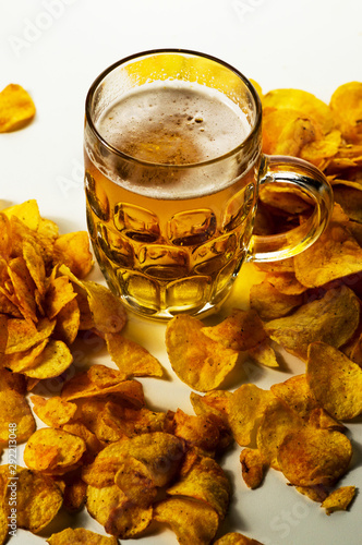 foamy beer in a transparent glass and a pile of potato chips on a white background photo