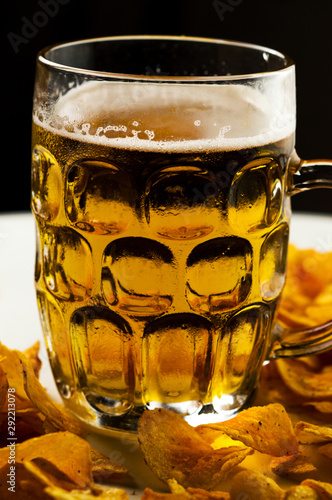 foamy beer in a transparent glass and a pile of potato chips on a white background photo