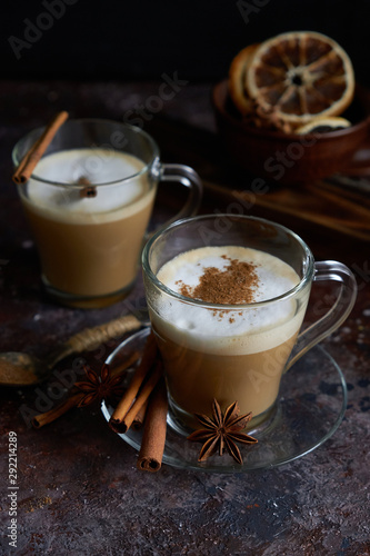 Two cups of hot cappuccino coffee with cinnamon and anise on a brown background
