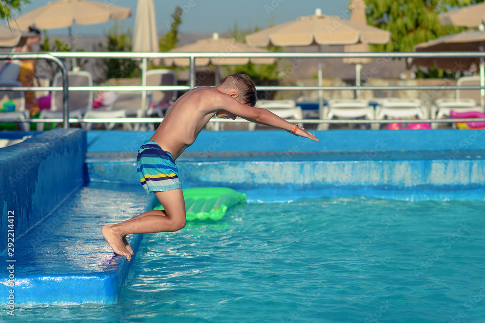 European boy in striped swimming shorts is diving to the swimming pool. He is enjoying his summer holidays in Spain.