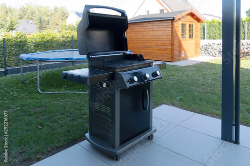 A large black gas grill stands on the street on the lawn near the house.