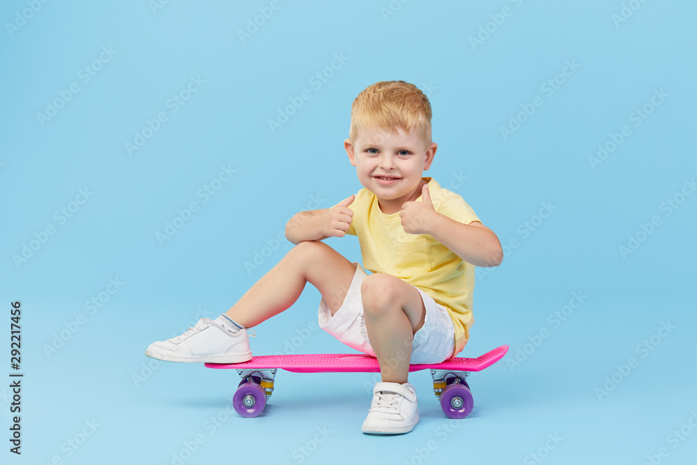 Stylish little toddler child boy in glasses with skateboard having fun over blue background Stylish little toddler child boy in glasses with skateboard having fun over blue background
