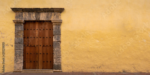 Facade of a colonial house in Cartagena with wooden door and coral stone with yellow or ocher wall