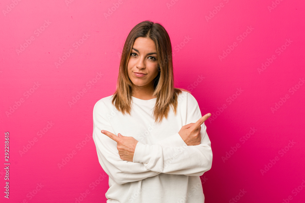Young authentic charismatic real people woman against a wall points sideways, is trying to choose between two options. Young authentic charismatic real people woman against a wall points sideways, is trying to choose between two options.