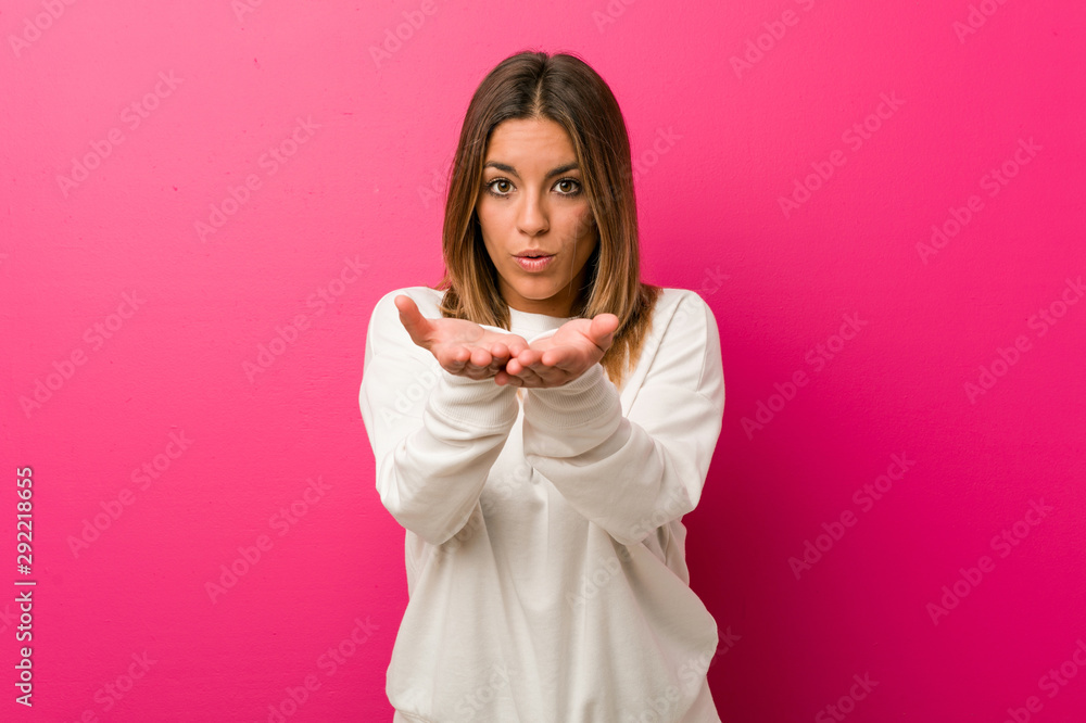 Young authentic charismatic real people woman against a wall folding lips and holding palms to send air kiss. Young authentic charismatic real people woman against a wall folding lips and holding palms to send air kiss.