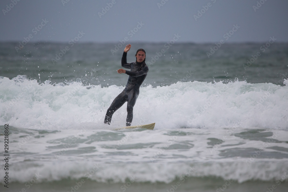 Side view of sportsman in black wetsuit surfing on white board in sea under gray sky Side view of sportsman in black wetsuit surfing on white board in sea under gray sky