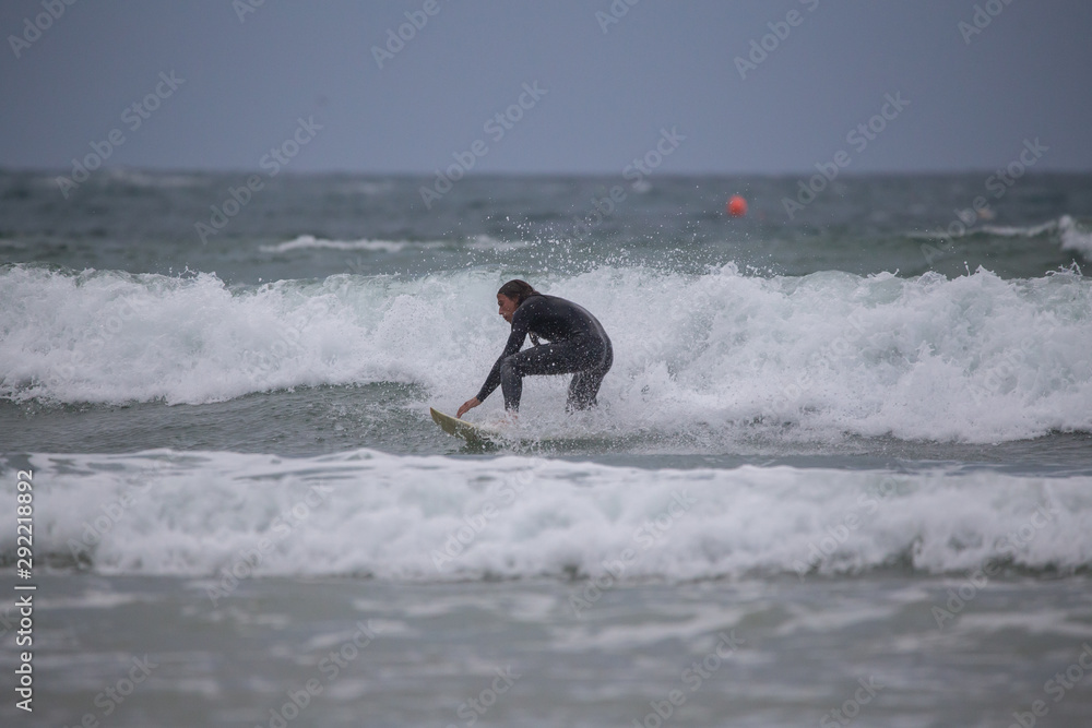 Side view of sportsman in black wetsuit surfing on white board in sea under gray sky Side view of sportsman in black wetsuit surfing on white board in sea under gray sky