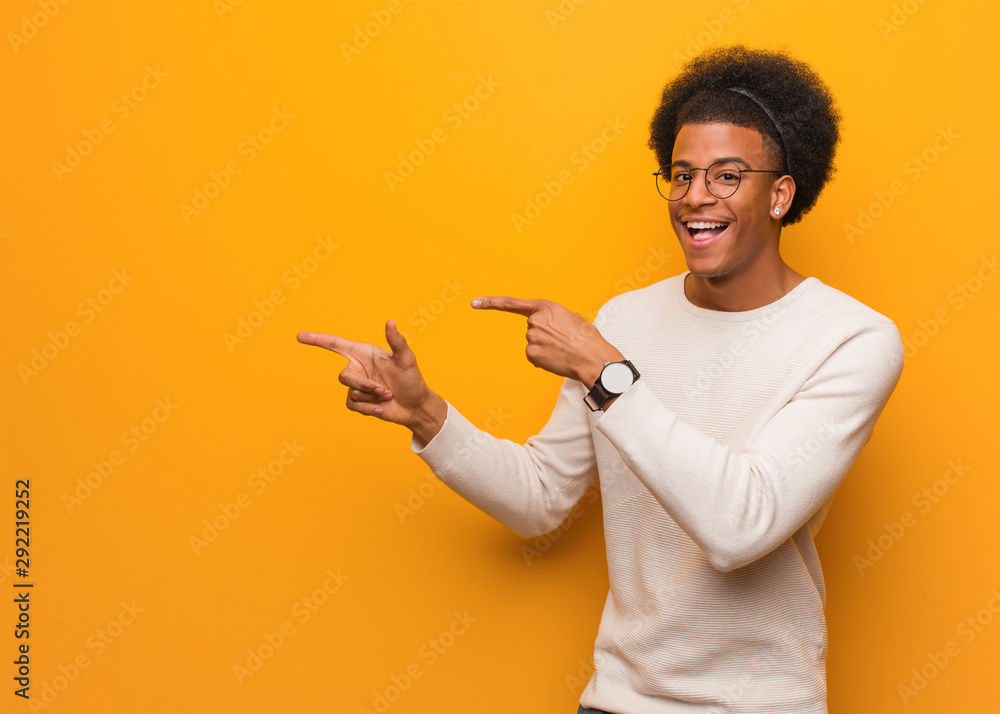 Young african american man over an orange wall pointing to the side with finger