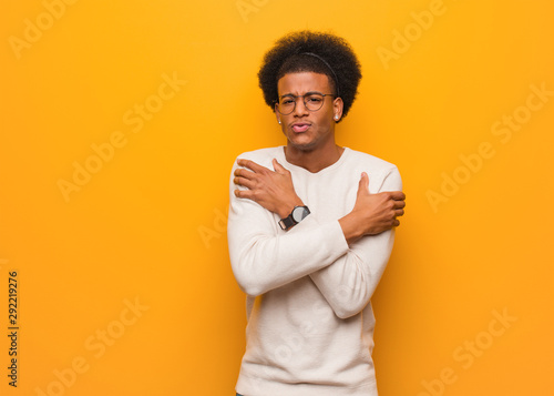 Young african american man over an orange wall going cold due to low temperature © Asier
