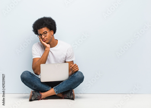 Young black man sitting on the floor with a laptop tired and very sleepy © Asier