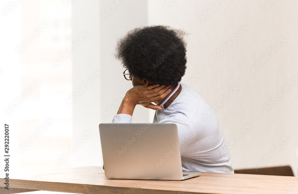 Young black man using his laptop from behind thinking about something Young black man using his laptop from behind thinking about something