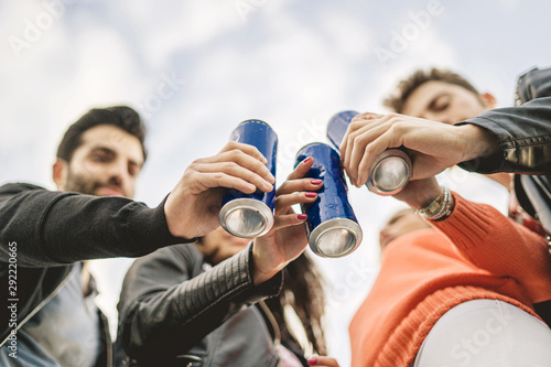 Group of young people toasting with canned beers outdoors. View from bottom, shallow depth of field with focus on the blue cans. Light sky in the background with some clouds. photo