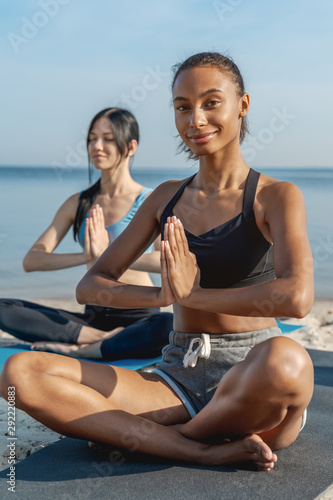 Vertical shot of female friends doing yoga exercise outdoors