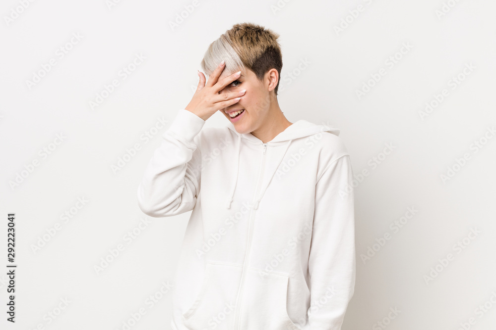 Young curvy woman wearing a white hoodie blink at the camera through fingers, embarrassed covering face. Young curvy woman wearing a white hoodie blink at the camera through fingers, embarrassed covering face.