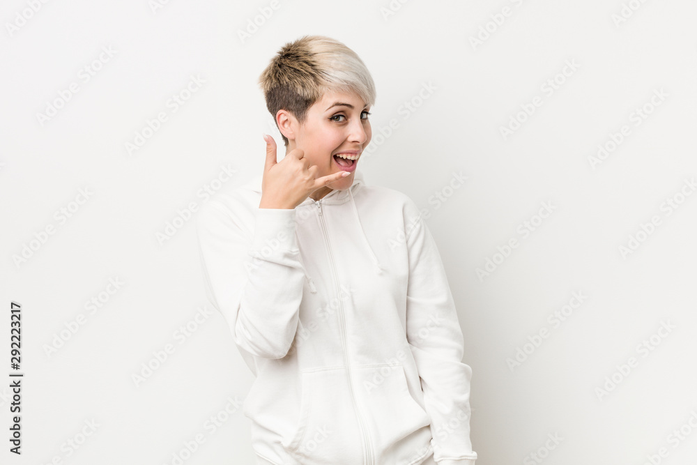 Young curvy woman wearing a white hoodie showing a mobile phone call gesture with fingers. Young curvy woman wearing a white hoodie showing a mobile phone call gesture with fingers.