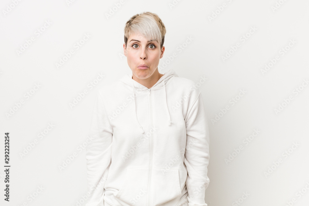 Young curvy woman wearing a white hoodie shrugs shoulders and open eyes confused. Young curvy woman wearing a white hoodie shrugs shoulders and open eyes confused.