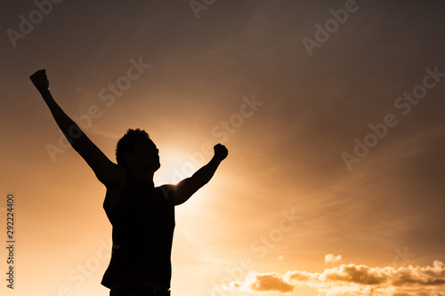 Young man feeling powerful and energized with arms up at sunset. 