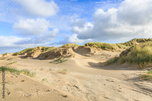 Dune valleys with deep wind holes carved out by heavy storm with swaying marram grasses with scattered clouds against blue sky