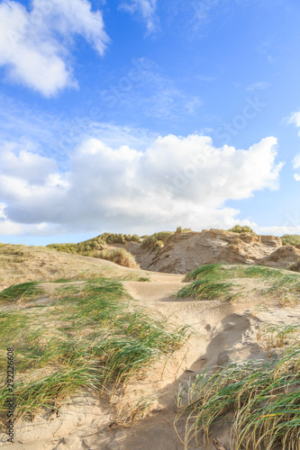 Dune valleys with deep wind holes carved out by heavy storm with swaying marram grasses with scattered clouds against blue sky