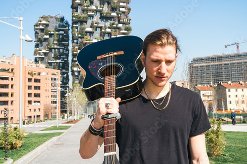 man holding guitar in his shoulder in front of two green skyscreapers photo