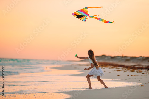 Little running girl with flying kite on tropical beach. Kid play on ocean shore.