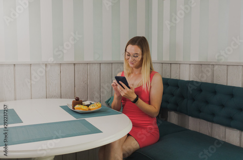 Beautiful girl sitting in a cafe with a phone in her hands and desserts on the table.