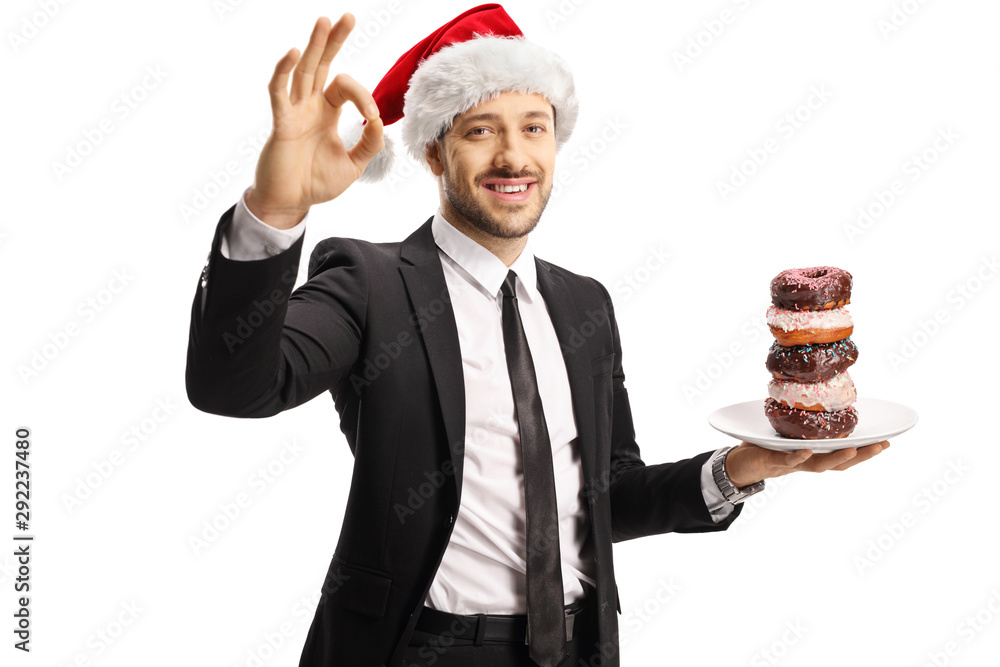 Businessman with a plate of donuts wearing a Santa Claus hat and gesturing sign perfect with fingers Businessman with a plate of donuts wearing a Santa Claus hat and gesturing sign perfect with fingers