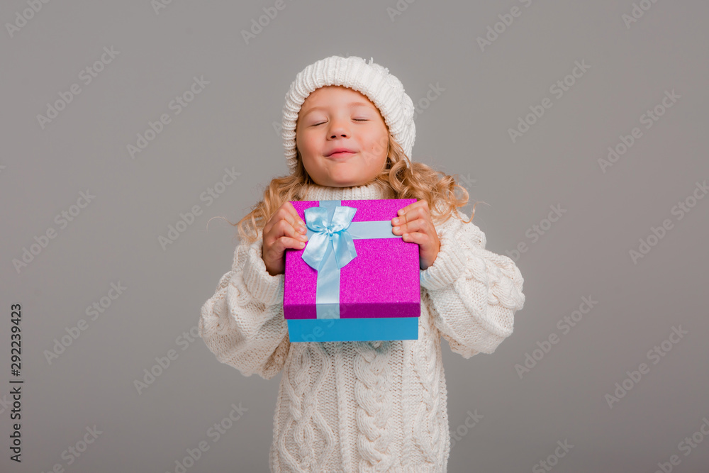 little blonde girl in winter white winter hat smiling holding a pink gift box