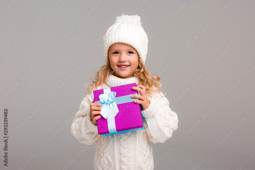 little blonde girl in winter white winter hat smiling holding a pink gift box little blonde girl in winter white winter hat smiling holding a pink gift box