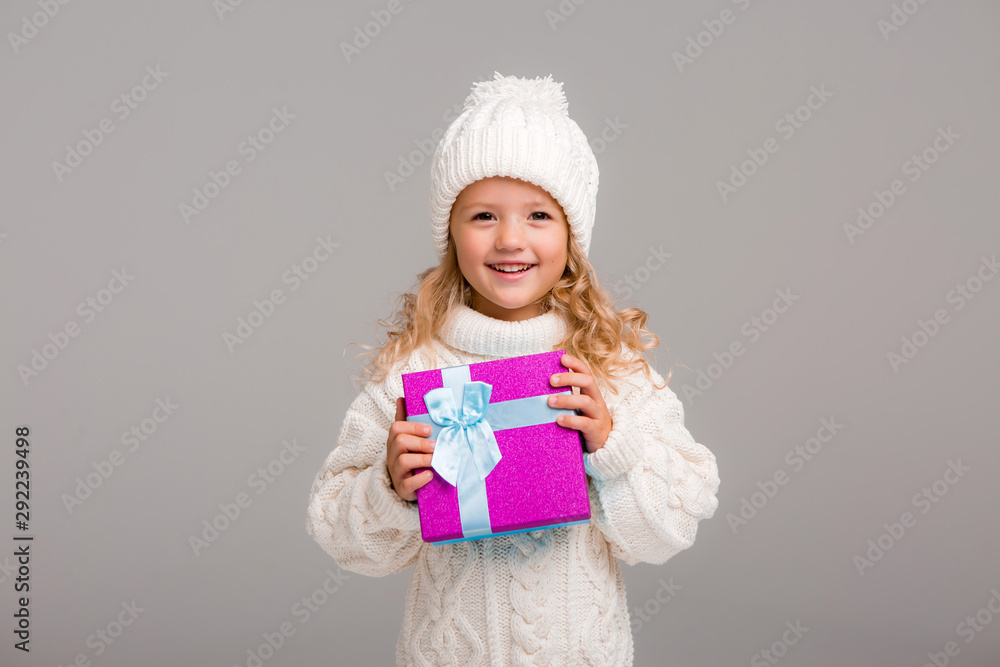 little blonde girl in winter white winter hat smiling holding a pink gift box little blonde girl in winter white winter hat smiling holding a pink gift box