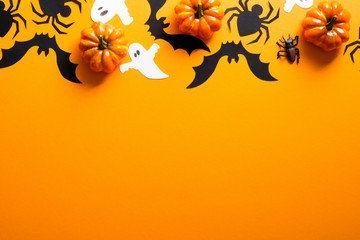 Happy halloween holiday concept. Halloween decorations, spiders, pumpkins, bats, ghosts on orange background. Halloween party greeting card mockup with copy space. Flat lay, top view, overhead.