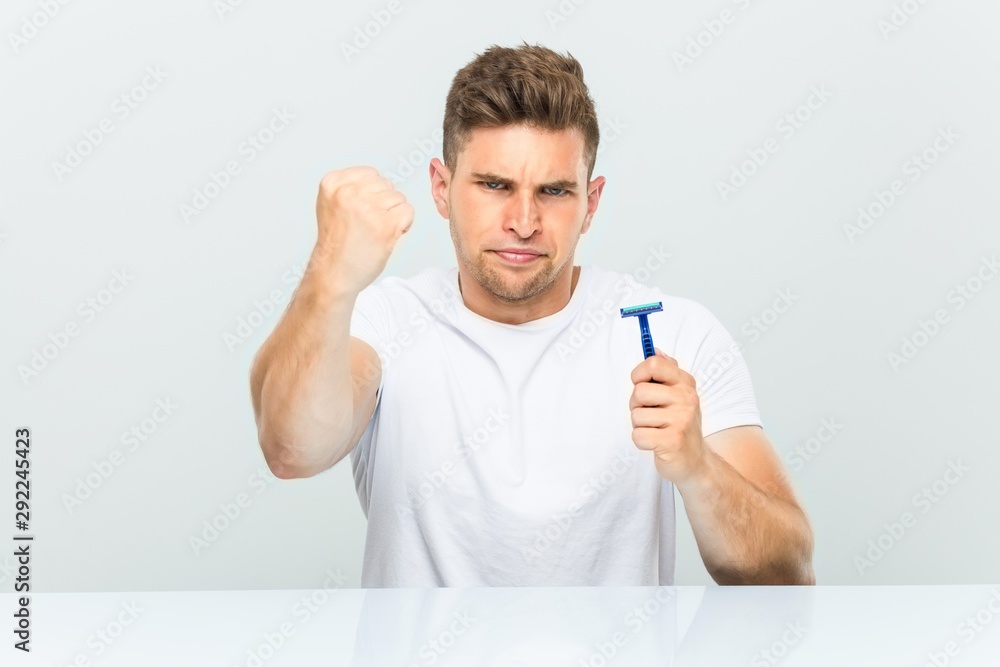 Young man holding a razor blade showing fist to camera, aggressive facial expression. Young man holding a razor blade showing fist to camera, aggressive facial expression.