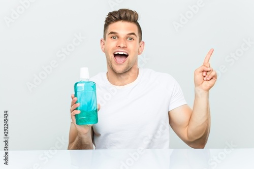 Young man holding a mouthwash smiling cheerfully pointing with forefinger away.