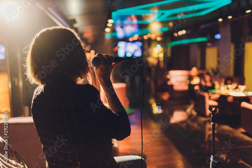 Obraz na plátně Young woman singing in karaoke and holding a microphone close-up