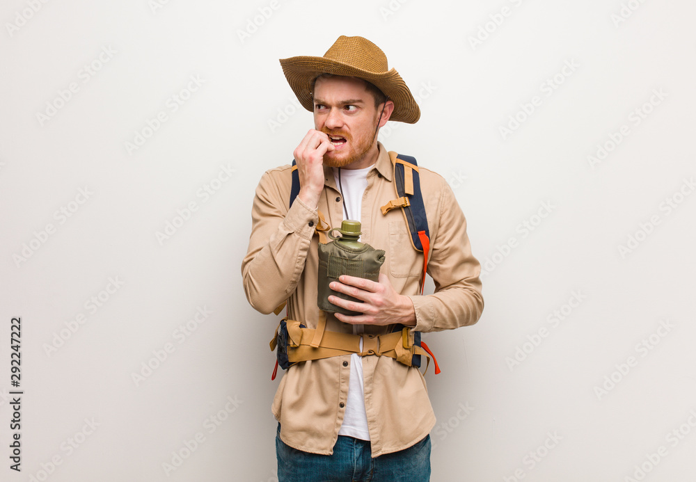 Young redhead explorer man biting nails, nervous and very anxious. He is holding a canteen. Young redhead explorer man biting nails, nervous and very anxious. He is holding a canteen.